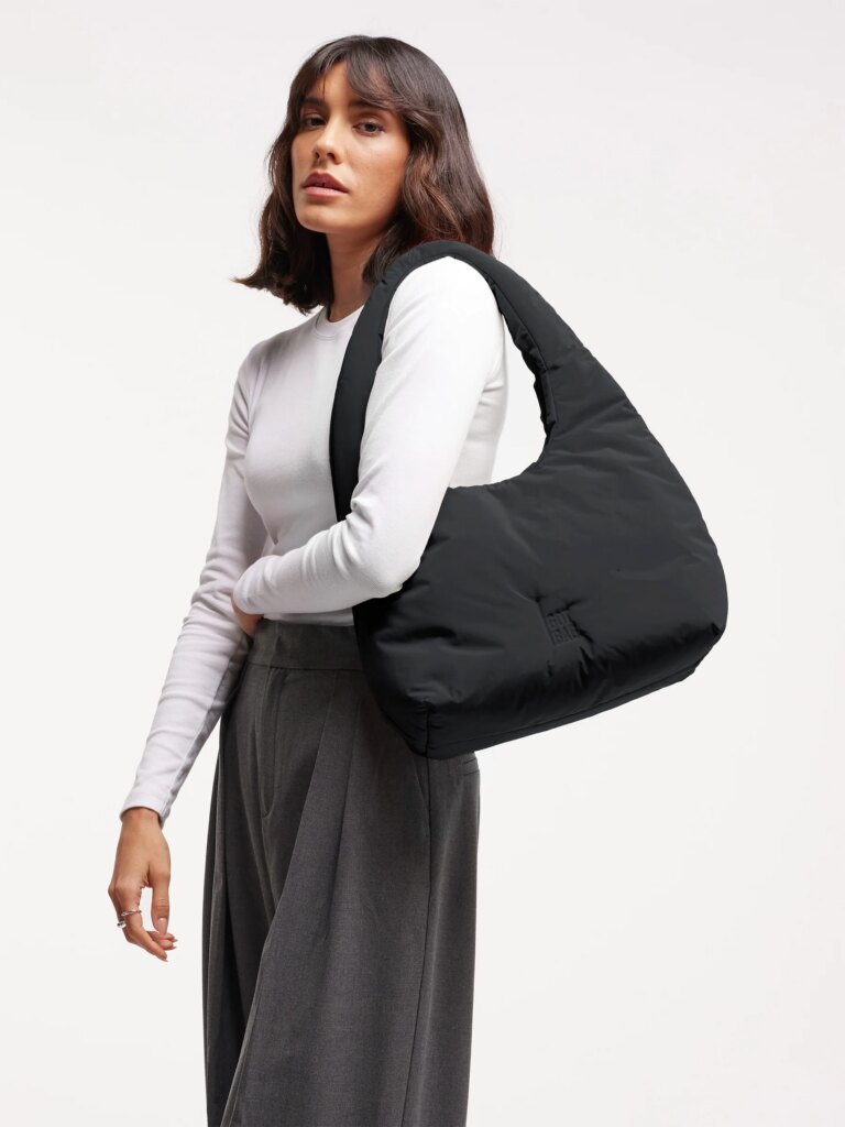 CLOUD SHOULDER BAG Tasche in black (Schwarz) von einer Frau über der Schulter getragen.