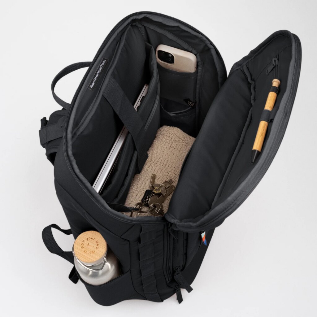 PRO PACK TRAVEL Rucksack in black (Schwarz) offen von oben gezeigt, gefüllt mit Laptop, Handy, Schlüssel, Stift, Wasserflasche. Label Made of Ocean Impact Plastic sichtbar.