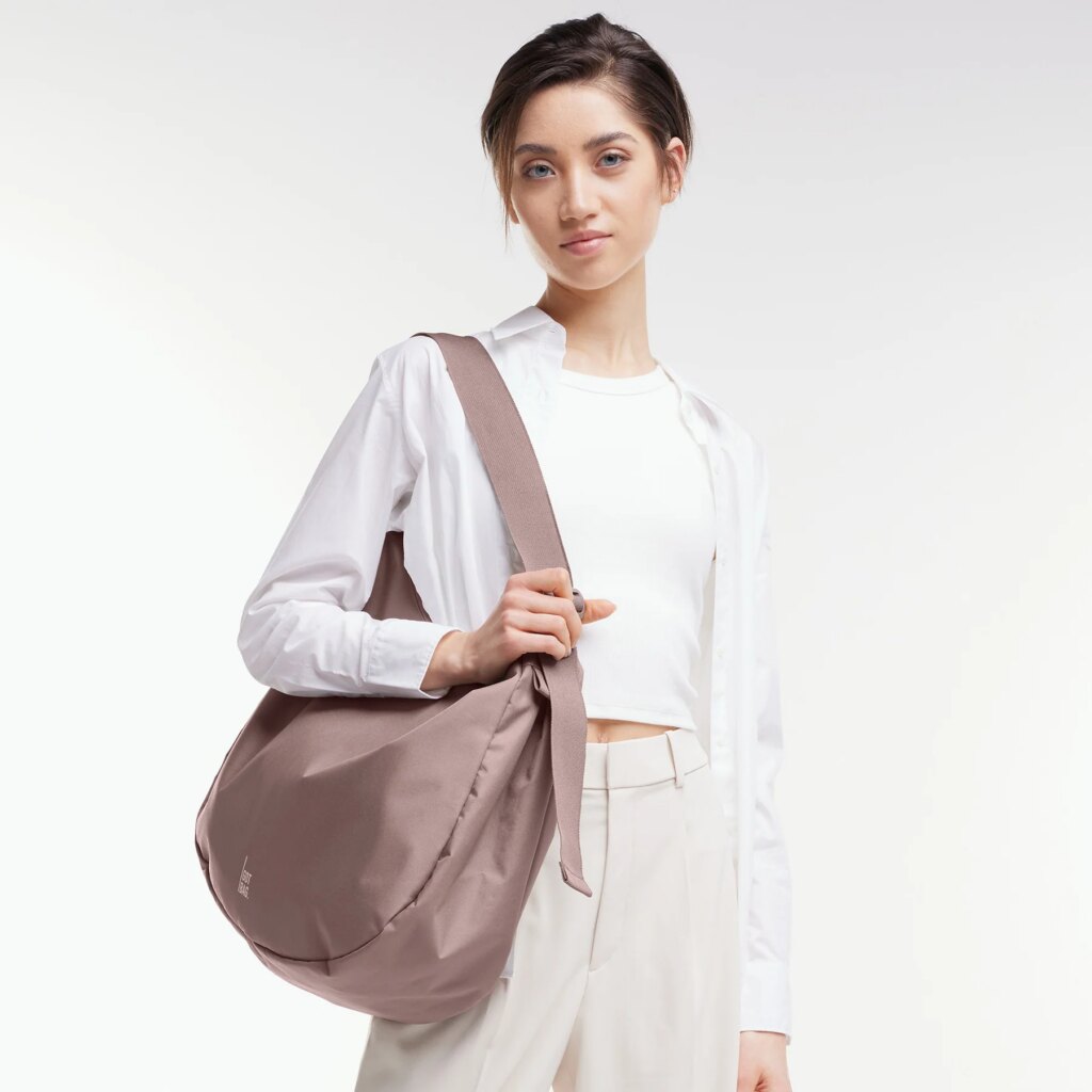 CURVED BAG Tasche in blobfish (dunkles Altrosa) von einer Frau über der Schulter getragen.