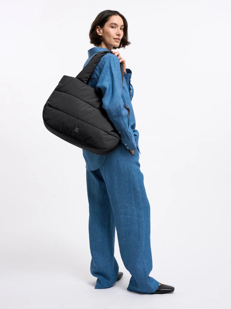 PUFFER HORIZON TOTE BAG Tasche in black (Schwarz) von einer Frau über der Schulter getragen.