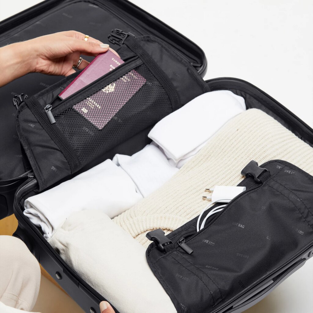RE-SHELL Cabin Koffer in black (Schwarz) von einer Person gepackt, ein Reisepass wird in eine Netztasche gelegt.