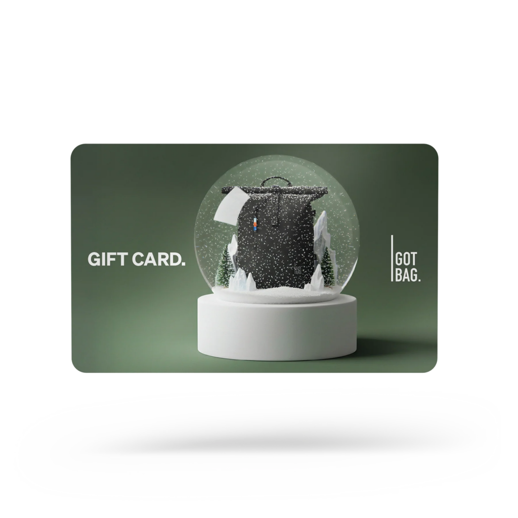 GIFT CARDS Accessoires: Eine dunkelgrüne Geschenkkarte mit einem Schneekugel-Design, das einen Rucksack im Schnee zeigt.