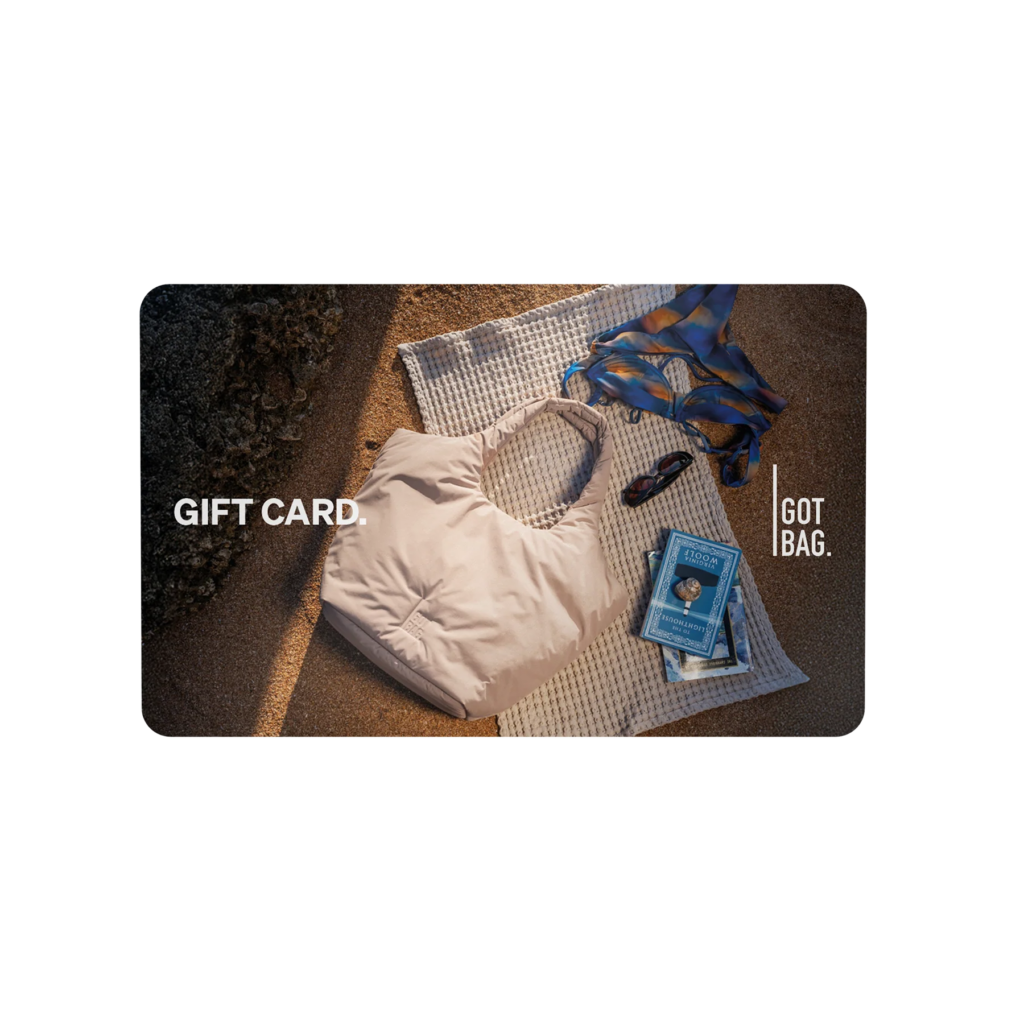 GIFT CARDS Accessoires mit Strandmotiv: helle Tasche, Sonnenbrille und Buch auf einem Handtuch im Sand.