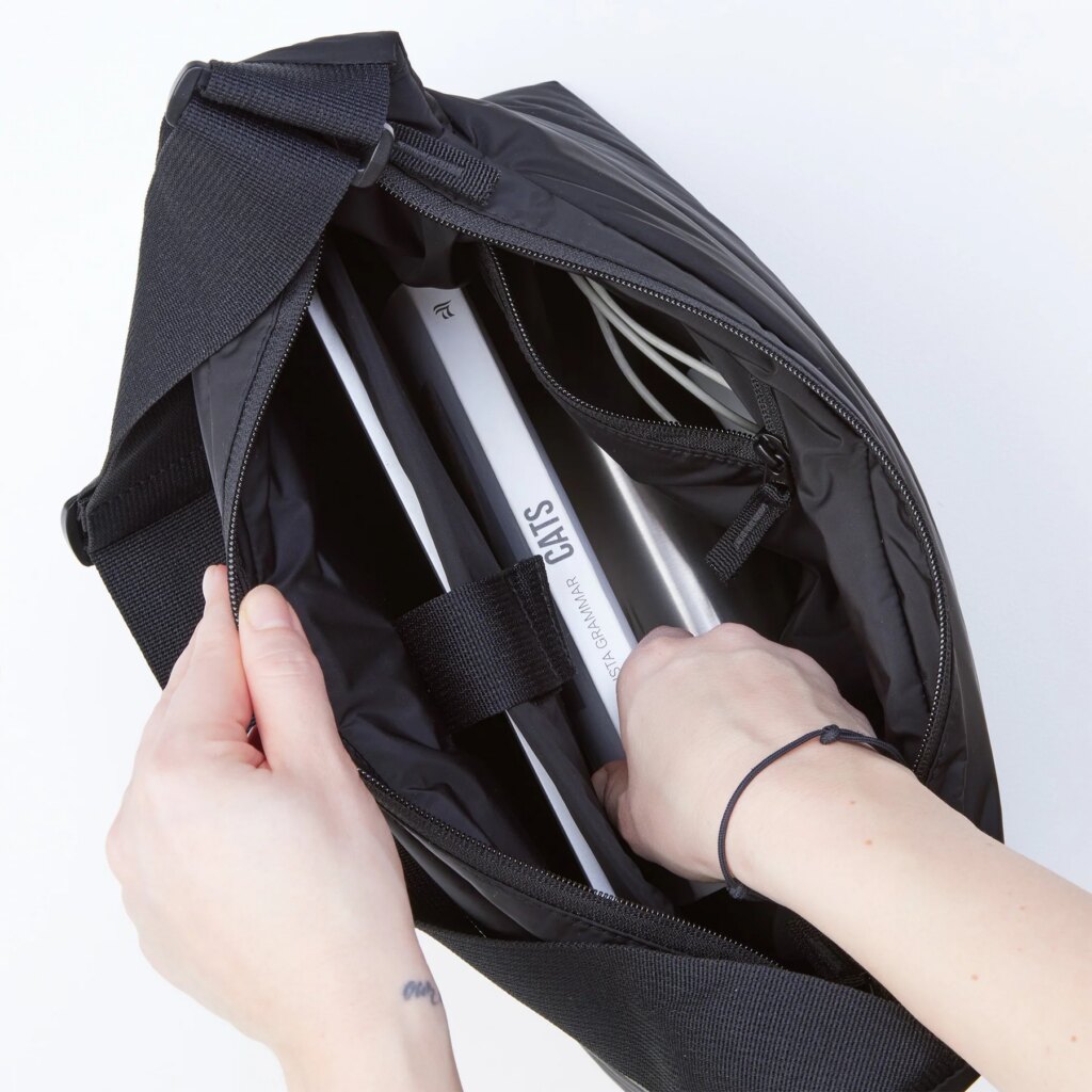 PUFFER SQUARE BAG Tasche in black (Schwarz), von einer Frau geöffnet und bestückt.