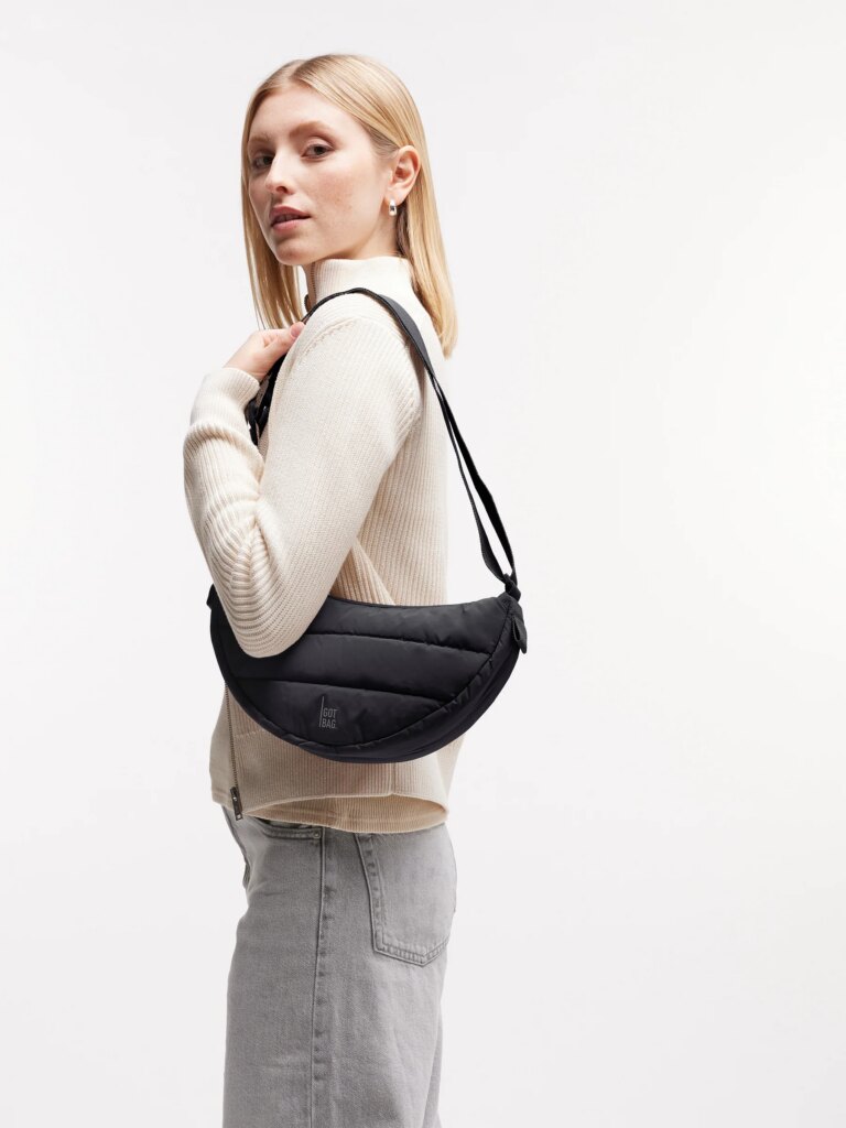 PUFFER MOON BAG SMALL Tasche in black (Schwarz) von einer Frau über der Schulter getragen.