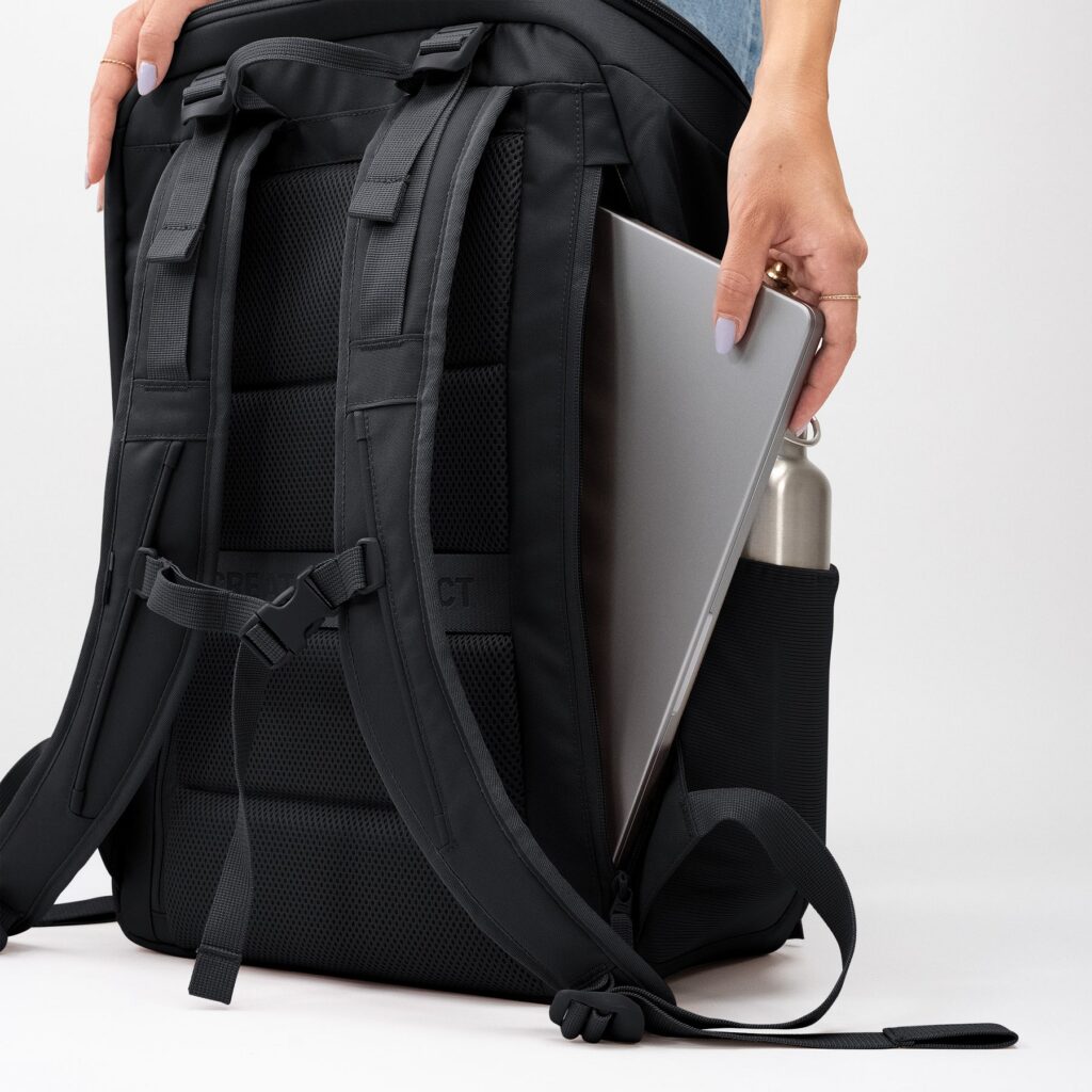PRO PACK TRAVEL Rucksack in black (Schwarz), eine Frau legt Laptop und Wasserflasche hinein.