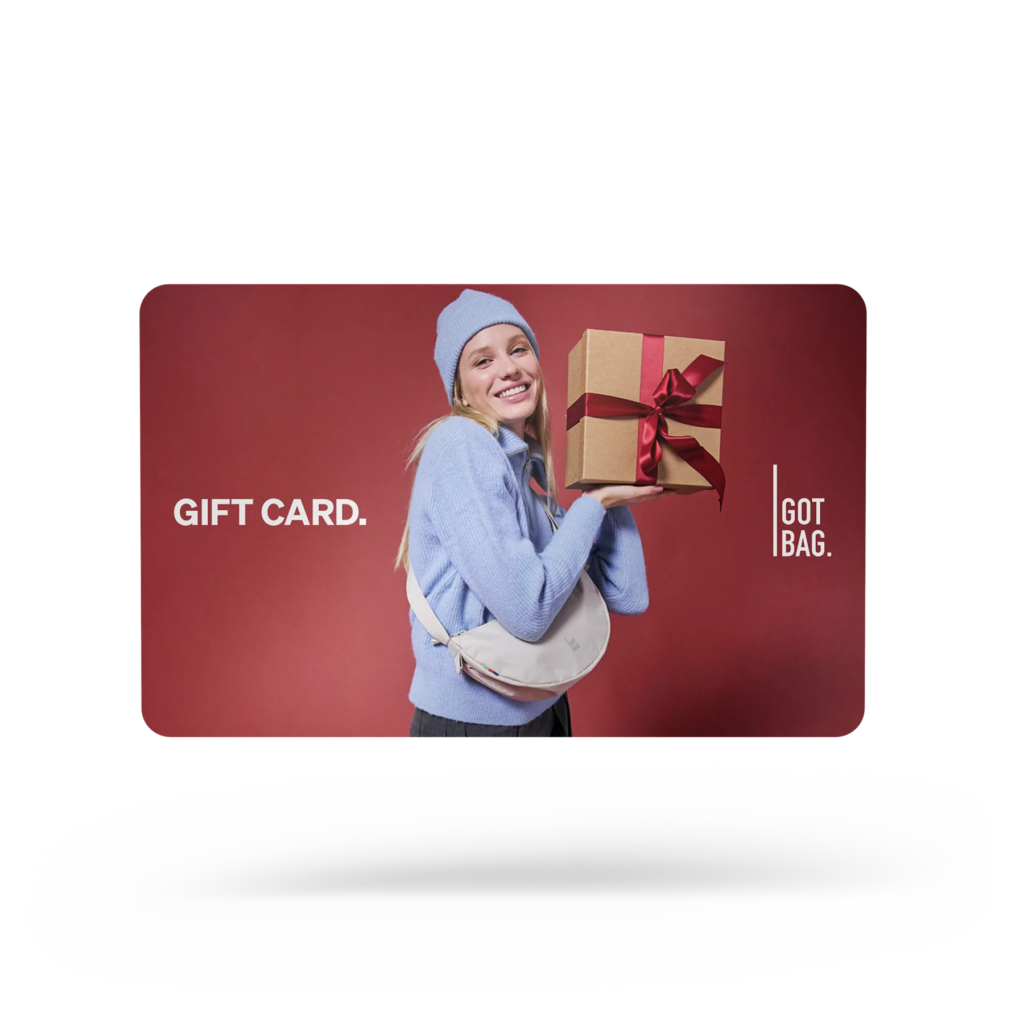 GIFT CARDS Accessoires, die eine lächelnde Frau in blauer Mütze und Pullover zeigt, die ein Geschenk hält.