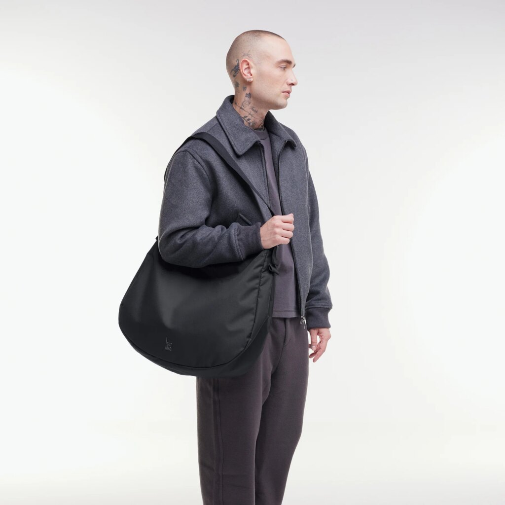 CURVED BAG Tasche in black (Schwarz) von einem Mann über der Schulter getragen.