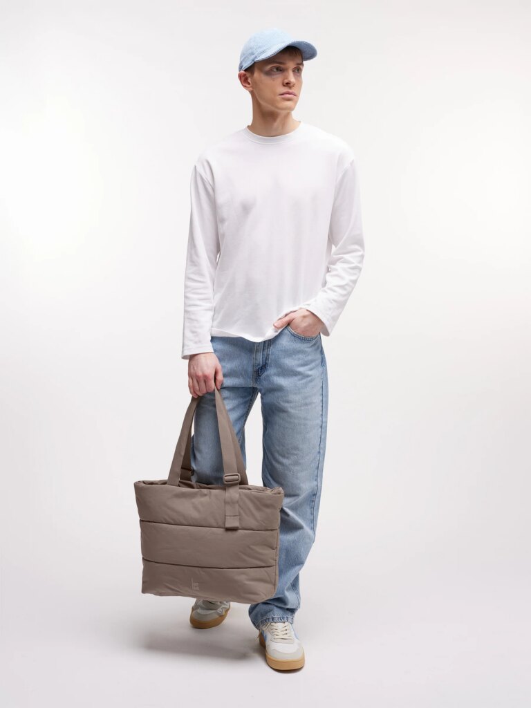 PUFFER TOTE BAG Tasche in oyster (klassisches Taupe-Braun) von einem Mann in der Hand gehalten.