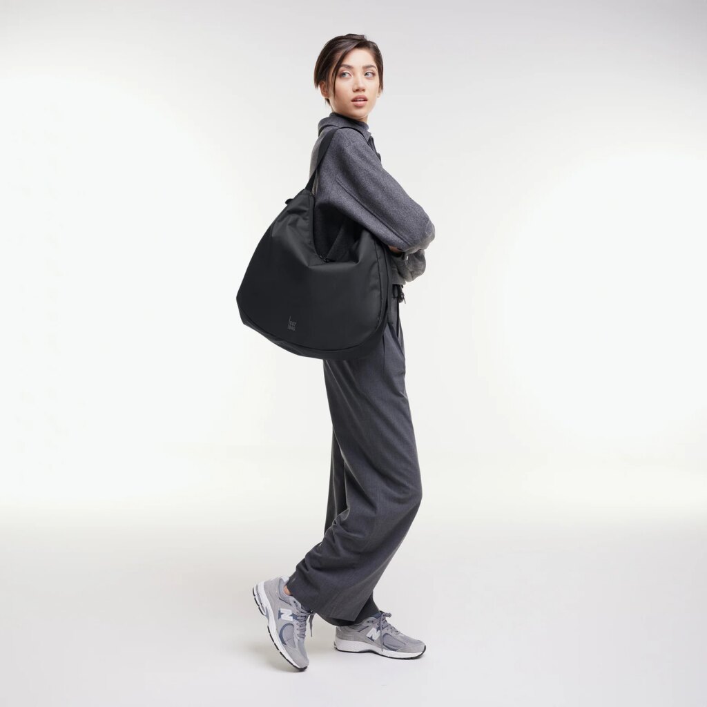 CURVED BAG Tasche in black (Schwarz) von einer Frau über der Schulter getragen.